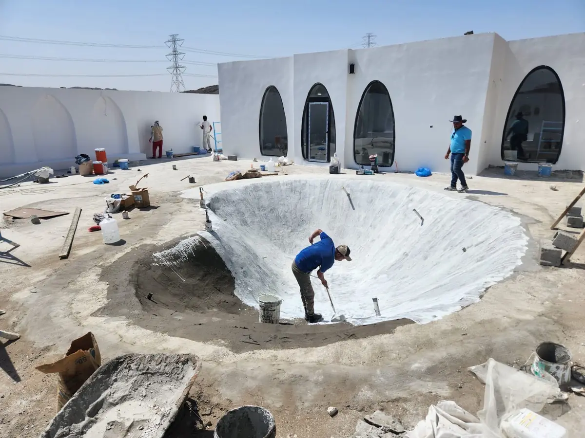 عامل يرشّ طبقة عزل بيضاء داخل حوض مسبح شاطئي قبل التشطيب النهائي